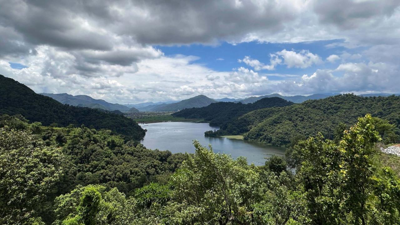 Winding blue reservoir through green forested hills under a cloudy sky